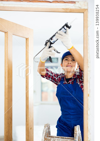 Female professional door installer fills gaps with mounting foam 139938254