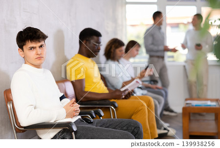 Dissatisfied young male visitor sitting on the bench in waiting room of clinic 139938256