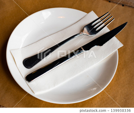 On paper tablecloth plate with cutlery, knife and fork complemented by transparent glass On paper tablecloth plate with cutlery, knife and fork complemented by transparent glass 139938336