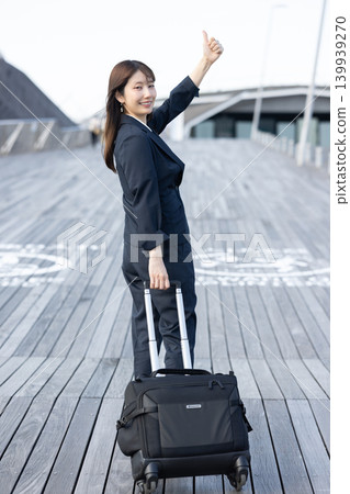 一位女商人拖著行李箱準備出差。 一位女商人拖著行李箱準備出差。 139939270