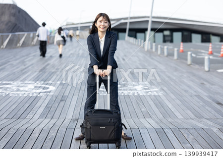 一位女商人拖著行李箱準備出差。 一位女商人拖著行李箱準備出差。 139939417