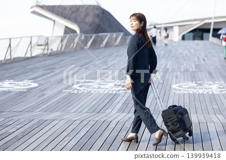 一位女商人拖著行李箱準備出差。 一位女商人拖著行李箱準備出差。 139939418