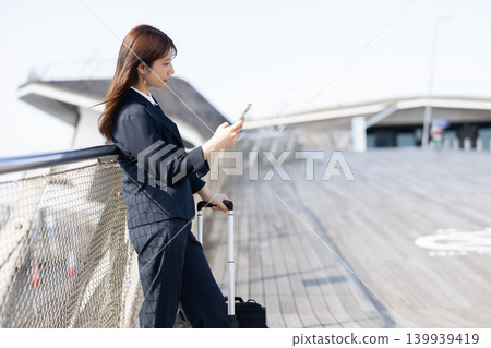 一位女商人拖著行李箱準備出差。 一位女商人拖著行李箱準備出差。 139939419