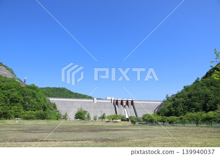 A panoramic view of the magnificent Tamagawa Dam in Tamagawa, Akita Prefecture, under a clear blue sky, and the water being released. A panoramic view of the magnificent Tamagawa Dam in Tamagawa, Akita Prefecture, under a clear blue sky, and the water being released. 139940037