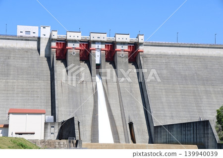 A panoramic view of the magnificent Tamagawa Dam in Tamagawa, Akita Prefecture, under a blue sky, and the water being released. A panoramic view of the magnificent Tamagawa Dam in Tamagawa, Akita Prefecture, under a blue sky, and the water being released. 139940039