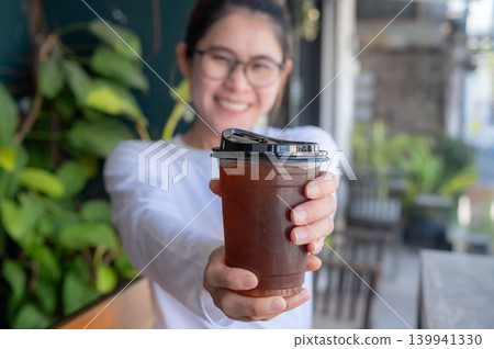 Asian woman holding an iced Americano coffee. An iced americano is a refreshing coffee drink made with espresso and cold water, served over ice. Asian woman holding an iced Americano coffee. An iced americano is a refreshing coffee drink made with espresso and cold water, served over ice. 139941330