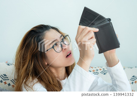 Asian woman trying to find money in her empty wallet. Having financial problems means being unable to pay debts over the short or long term. Asian woman trying to find money in her empty wallet. Having financial problems means being unable to pay debts over the short or long term. 139941332