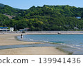 A woman stands in the distance at the tranquil waterfront of Chichibugahama beach, with the lush green mountains as her backdrop (Kagawa Prefecture). 139941436