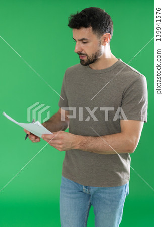 Adult man making notes on paper documents in front of green screen 139941576