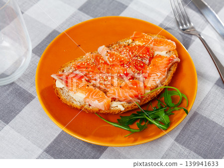 On table there is plate with light snack - toast, crispy salmon sandwiches with rucola and sesame On table there is plate with light snack - toast, crispy salmon sandwiches with rucola and sesame 139941633