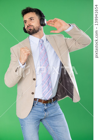 Adult man listening to music with headphones in front of green screen Adult man listening to music with headphones in front of green screen 139941654