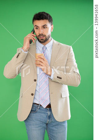 Adult man talking on phone and drinking coffee in front of green screen Adult man talking on phone and drinking coffee in front of green screen 139941658