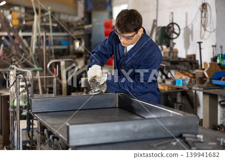 Young worker uses an angle grinder while working at mechanical engineering plant 139941682