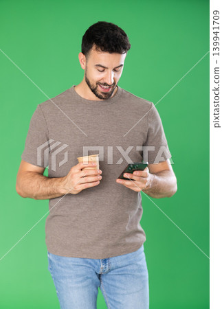 Adult man scrolling smartphone and drinking coffee in front of green screen Adult man scrolling smartphone and drinking coffee in front of green screen 139941709