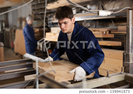 Young guy putting wooden board on cutting machine Young guy putting wooden board on cutting machine 139941873