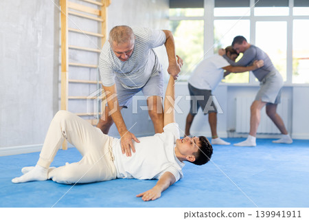 Guy and senior man athletes in pair conduct training battle in oriental fighting technique Guy and senior man athletes in pair conduct training battle in oriental fighting technique 139941911
