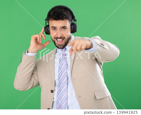 Adult man listening to music with headphones in front of green screen Adult man listening to music with headphones in front of green screen 139941925