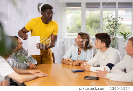Middle-aged man instructor explaining the topic to group of guys around the table Middle-aged man instructor explaining the topic to group of guys around the table 139941954