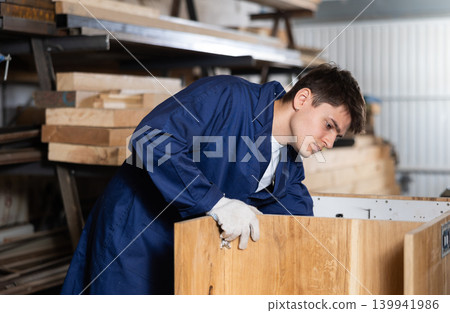 Young guy assembling wooden cabinet in workshop Young guy assembling wooden cabinet in workshop 139941986