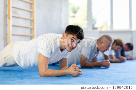 Group of men doing muscle stretching before boxing or judo class - doing gymnastic exercise plank 139942015