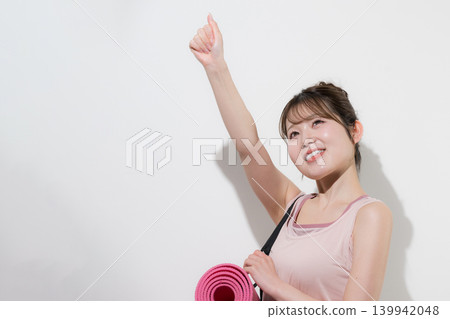 A healthy and beautiful woman holding a yoga mat against a white background, training in a gym or lifestyle setting. A healthy and beautiful woman holding a yoga mat against a white background, training in a gym or lifestyle setting. 139942048
