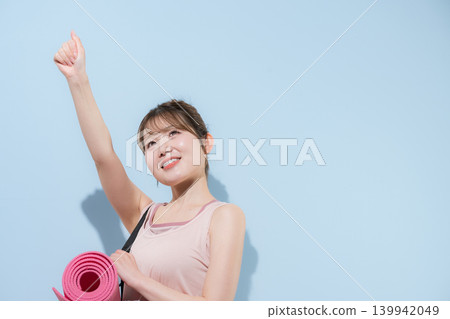 A woman holding a yoga mat against a light blue background, representing a healthy and beautiful sport, training at a gym, or lifestyle. A woman holding a yoga mat against a light blue background, representing a healthy and beautiful sport, training at a gym, or lifestyle. 139942049