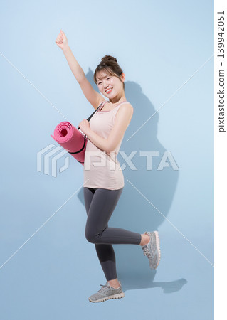 A woman holding a yoga mat against a light blue background, representing a healthy and beautiful sport, training at a gym, or lifestyle. A woman holding a yoga mat against a light blue background, representing a healthy and beautiful sport, training at a gym, or lifestyle. 139942051