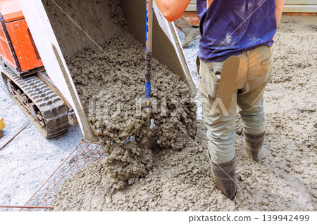 Workers are pouring concrete from tracked wheelbarrow onto ground for building purposes 139942499
