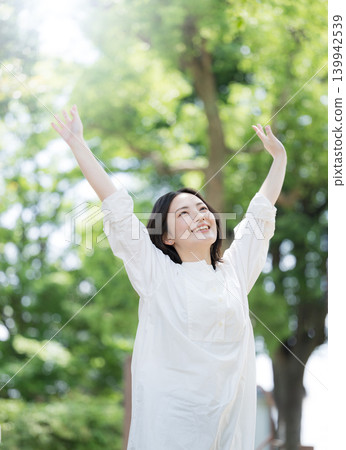 A healthy lifestyle image of a woman refreshing herself by taking a deep breath amidst the fresh greenery of nature. 139942539