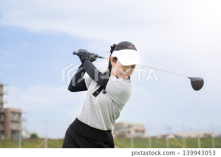 一張年輕女高爾夫球手在練習場揮桿的運動照片。 一張年輕女高爾夫球手在練習場揮桿的運動照片。 139943053
