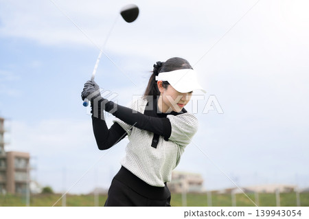 一張年輕女高爾夫球手在練習場揮桿的運動照片。 一張年輕女高爾夫球手在練習場揮桿的運動照片。 139943054