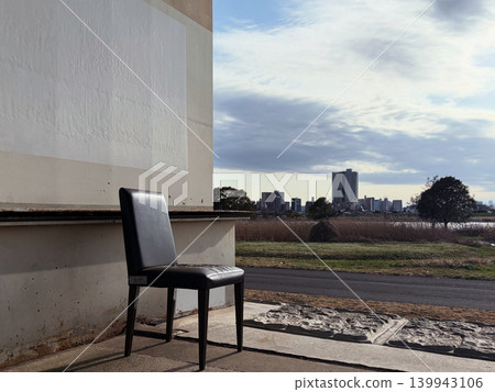 A single black chair stands alone along the riverbank, beside the buildings. A single black chair stands alone along the riverbank, beside the buildings. 139943106