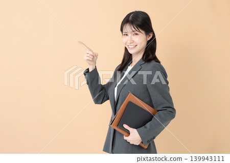 A smiling businesswoman holding a file and pointing. A smiling businesswoman holding a file and pointing. 139943111