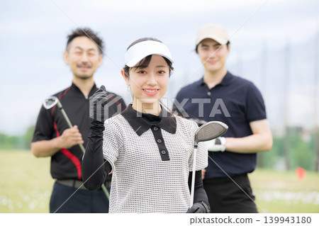 一位正在學習打高爾夫球的女士面帶微笑，擺出勝利的姿勢；她和她的高爾夫教練及朋友們一起享受著健康的生活方式，並對鏡頭露出笑容。 139943180
