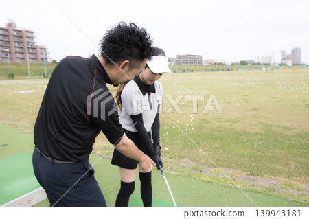 一位微笑的女士正在學習高爾夫球;這是她接受高爾夫教練揮桿指導的圖片。 一位微笑的女士正在學習高爾夫球;這是她接受高爾夫教練揮桿指導的圖片。 139943181