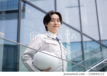 A young male engineer smiles against a backdrop of city buildings, representing a construction career image: job hunting, career, growth, and challenges. A young male engineer smiles against a backdrop of city buildings, representing a construction career image: job hunting, career, growth, and challenges. 139944137