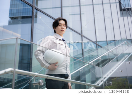 A young male engineer with a serious expression stands against a backdrop of city buildings, symbolizing a construction career, job hunting, career development, and personal growth. A young male engineer with a serious expression stands against a backdrop of city buildings, symbolizing a construction career, job hunting, career development, and personal growth. 139944138