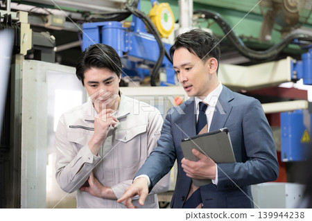 In a manufacturing plant, technicians in work clothes and sales staff are looking at the machinery and discussing estimates, repair costs, and maintenance fees. In a manufacturing plant, technicians in work clothes and sales staff are looking at the machinery and discussing estimates, repair costs, and maintenance fees. 139944238