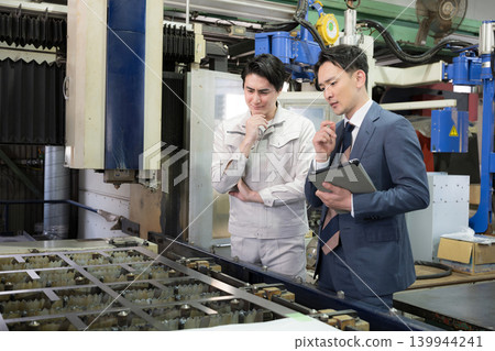 In a manufacturing plant, technicians and salespeople in work clothes are looking at the machinery and pondering the costs of estimates, repairs, and maintenance. 139944241