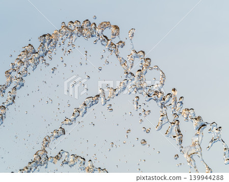 Splashes and jets of water against light background. Splashes and jets of water against light background. 139944288