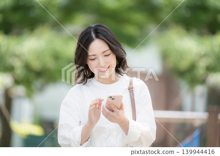 A lifestyle image of a woman using her smartphone outdoors amidst fresh greenery, such as searching for a map. A lifestyle image of a woman using her smartphone outdoors amidst fresh greenery, such as searching for a map. 139944416