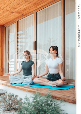Two young caucasian woman meditating on a wooden terrace at home Two young caucasian woman meditating on a wooden terrace at home 139944530