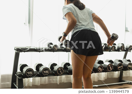 Rear view of woman exercise doing dumbbell kickbacks at the gym. Rear view of woman exercise doing dumbbell kickbacks at the gym. 139944579