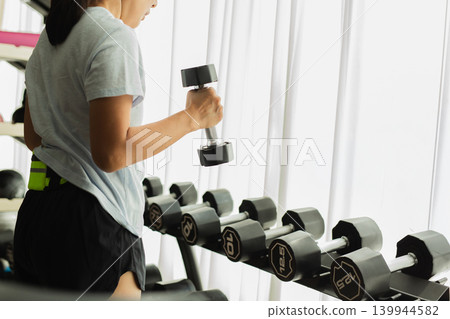 Side view of woman holding a dumbbell during a workout at gym. 139944582