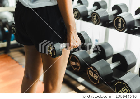 Rear view of woman holding a dumbbell doing weight training exercise at the gym. Rear view of woman holding a dumbbell doing weight training exercise at the gym. 139944586