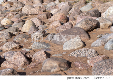 Sunlit rocky beach covered with smooth granite stones and sandy patches Sunlit rocky beach covered with smooth granite stones and sandy patches 139944998
