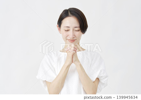 A middle-aged woman praying against a white background. A middle-aged woman praying against a white background. 139945634