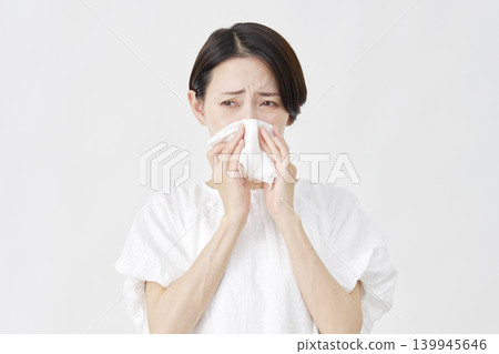 Middle-aged woman blowing her nose against a white background. 139945646