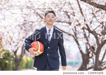 一名籃球隊的男學生沿著一排櫻花樹走著。 一名籃球隊的男學生沿著一排櫻花樹走著。 139945806