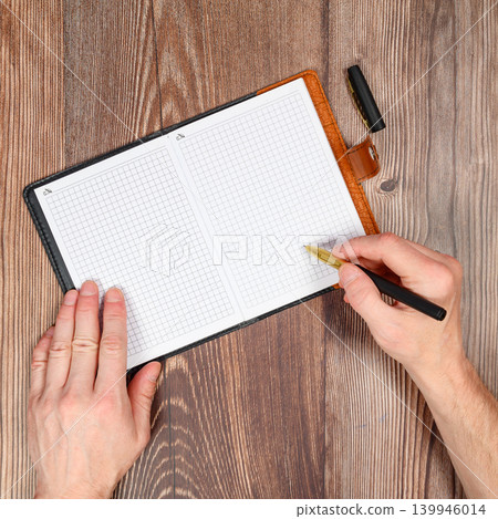 two human hands are resting on an open notebook with a pen on the table 139946014